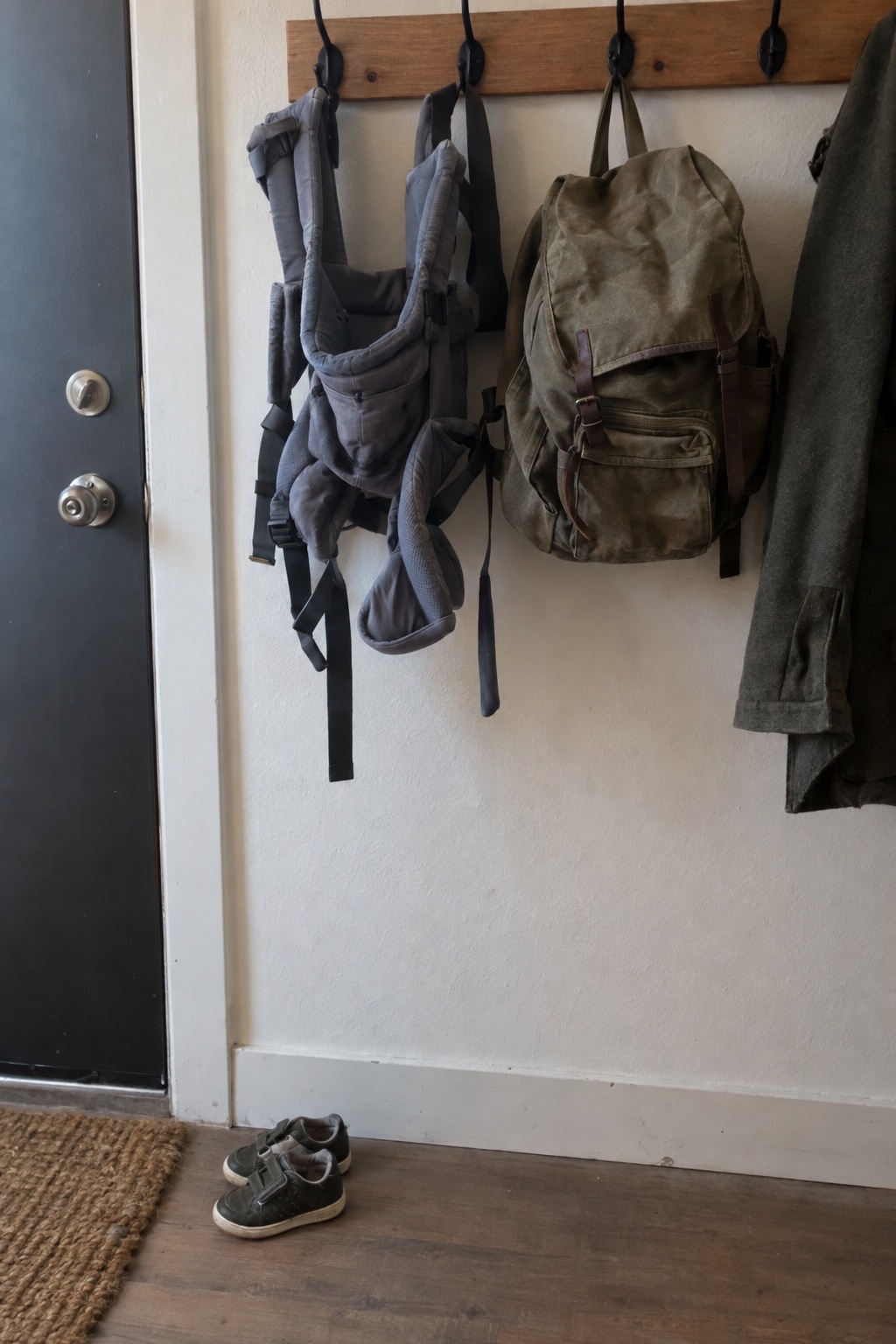 A baby carrier and a canvas backpack on hooks by the door